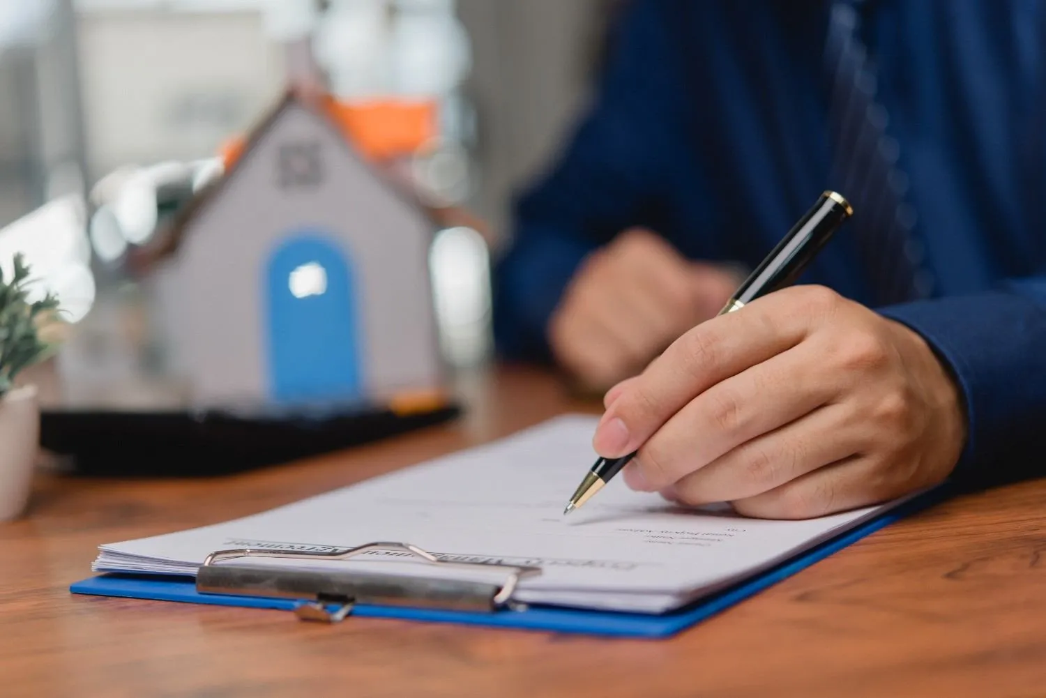 Homeowner signing a home warranty contract beside a small model house